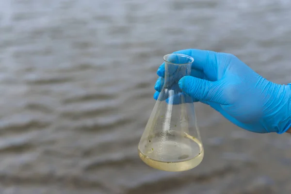 Analiz için nehirden örnek su. Bir test tüpü tutan eldiven. Ekoloji konsepti.