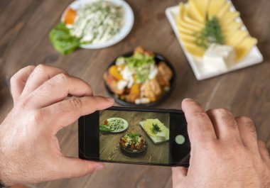 Gıda blogger fotoğraf çekmek akıllı telefon kullanarak . Mans eller geleneksel yemekler telefon fotoğrafçılığı yapmak. öğle yemeği ya da akşam yemeği et ve patates. Sosyal medya için, bloglama. En iyi görüntü cep telefonu.