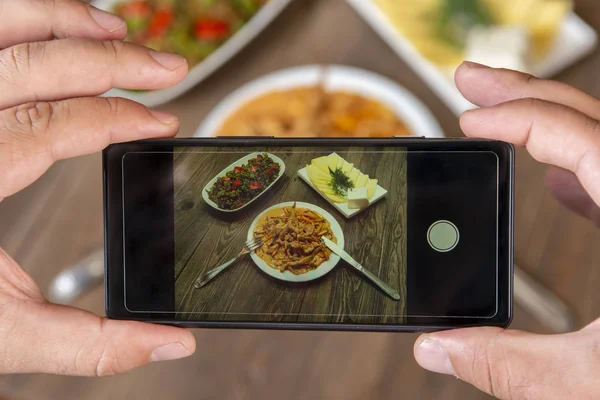 Yemeklerin akıllı telefon fotoğrafı. İnsan elleri, geleneksel yemeklerin fotoğrafını çeker. Öğle ya da akşam yemeği. Sığır stroganoff. Sosyal medya ve blog için. Üst görünüm cep telefonu.