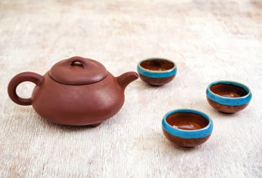 Kahverengi kil çaydanlık ve hafif ahşap zemin üzerinde fincanlar