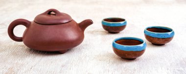 Kahverengi kil çaydanlık ve hafif ahşap zemin üzerinde fincanlar