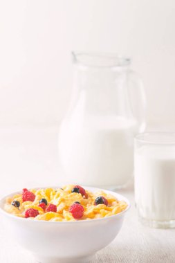 Beyaz arka planda ahududu ve yaban mersinli mısır gevreği. Kahvaltı. Böğürtlenli ve sütlü mısır gevreği. Mısır gevreği. Taze sağlıklı yiyecekler. Sabah yemeği. Tahta masa. Organik. Diyet kavramı.