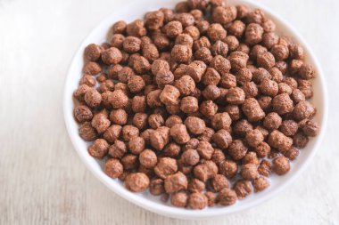 Beyaz ahşap arka planda çikolatalı mısır topu ve süt dolu bir kase..