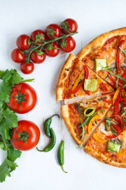 Peynirli, domatesli, biberli ve ahşap masadaki avokadolu vejetaryen pizzası.