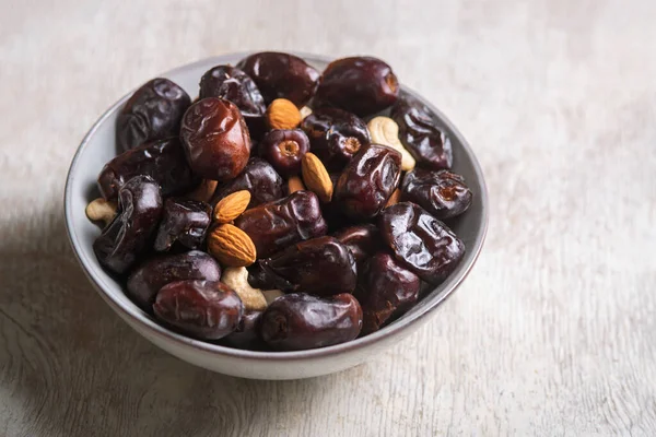 Beyaz ahşap arka planda fındık ve hurma karışımı sağlıklı yiyecekler.