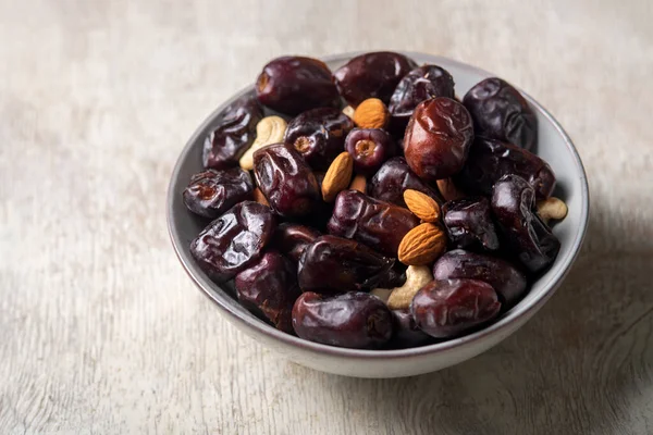 Beyaz ahşap arka planda fındık ve hurma karışımı sağlıklı yiyecekler.