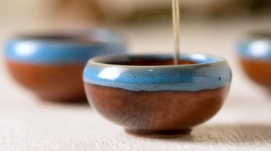 Person pouring tea from a Chinese teapot in a cup , tea spills on the table. Slow motion