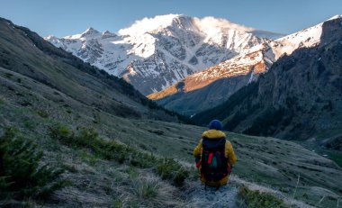 Bir adam oturur ve dağlarda sabah şafağına bakar..