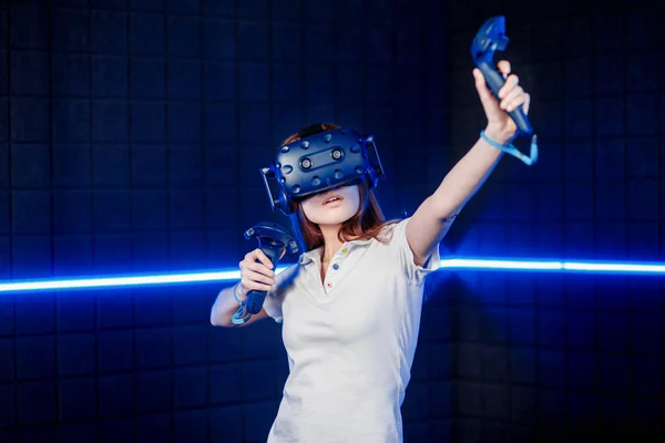 Una joven en un casco de realidad virtual en la sala de juegos está jugando un videojuego . — Foto de Stock