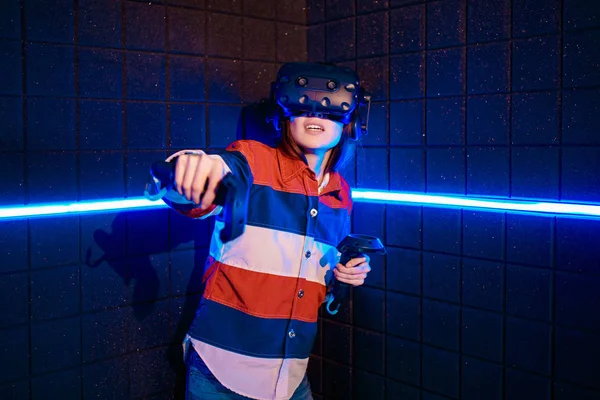 Uma jovem em um capacete de realidade virtual na sala de jogos está jogando um jogo de vídeo . — Fotografia de Stock