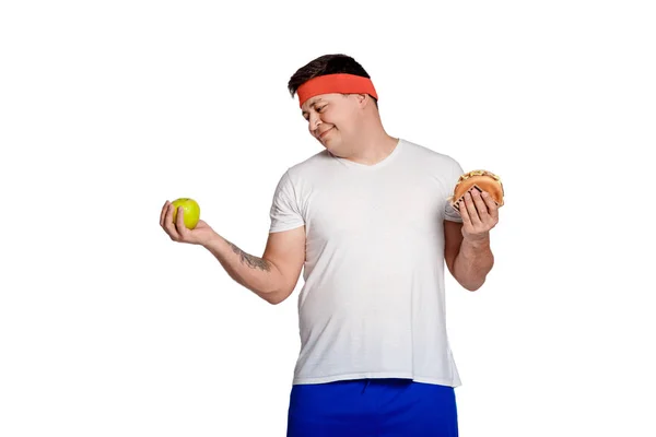 Homem gordo não pode escolher entre um hambúrguer e uma maçã . — Fotografia de Stock