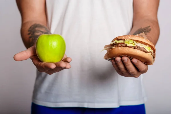 concept man makes the choice between healthy and unhealthy food. the choice between a burger and an apple. will power when dieting.