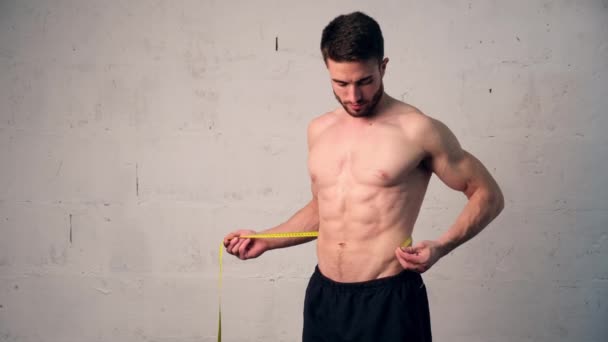 En ung man med idrottsfysik mäter midjan, kollar hur mycket han har gått ner i vikt. viktminskning, män lever en — Stockvideo