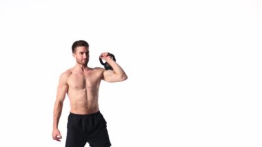Sakallı, atletik yapılı genç adam beyaz bir arka planda fitness yapıyor. Fitness antrenörü ağırlık kaldırır