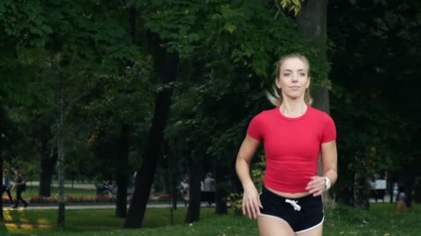 Een jong meisje met een rood topje loopt in het park. joggen slow motion, fitness buiten. meisje haar paardenstaart — Stockvideo