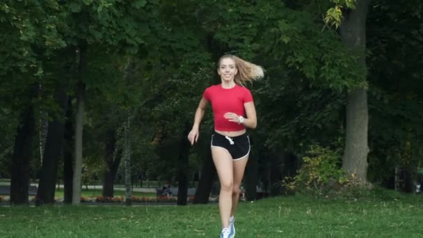 Een jong meisje met een rood topje loopt in het park. joggen slow motion, fitness buiten. meisje haar paardenstaart — Stockvideo