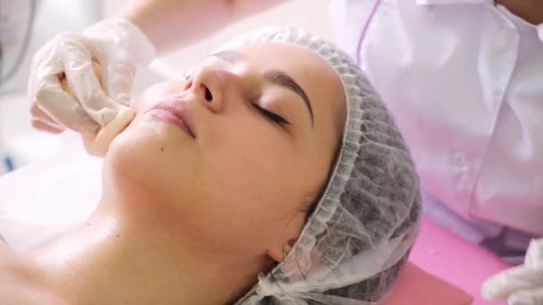 Specialista di cosmetologia che applica la maschera facciale con il pennello, rendendo la pelle idratata e sana. Donna attraente rilassante — Video Stock