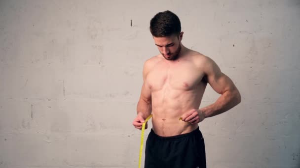 En ung man med idrottsfysik mäter midjan, kollar hur mycket han har gått ner i vikt. viktminskning, män lever en — Stockvideo