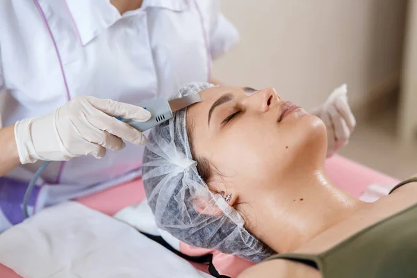 Beauty Specialist Makes Ultrasonic Peeling For Female Client\'s Face. Cosmetologist doing procedure of cleaning face with ultrasonic scrubber. In beauty salon
