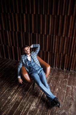 Mavi takım elbiseli başarılı genç işadamı deri bir sandalyede oturuyor. Sakallı genç adam gülümsüyor..