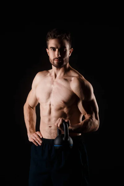O homem bearded novo com um kettlebell em suas mãos em um fundo preto. atleta nu-chested — Fotografia de Stock