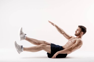 Spor fiziği olan genç bir adam, beyaz izole edilmiş bir arka planda karın boşluğu kasları üzerinde egzersiz yapar, sporcu spor için gider, basın kasları üzerinde egzersiz yapar.
