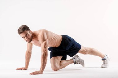 Spor fiziği olan genç bir adam, beyaz izole edilmiş bir arka planda karın boşluğu kasları üzerinde egzersiz yapar, sporcu spor için gider, basın kasları üzerinde egzersiz yapar.