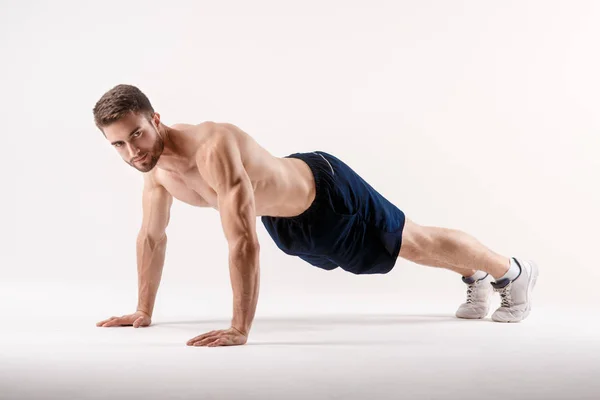 Ung man med skägg av en sport fysik gör armhävningar från golvet på en vit isolerad bakgrund, idrottsman går in för sport — Stockfoto