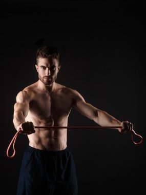 Elinde jimnastik lastikleri olan siyah arka planda sakallı bir sporcu.
