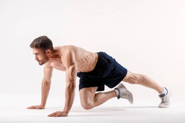 Spor fiziği olan genç bir adam, beyaz izole edilmiş bir arka planda karın boşluğu kasları üzerinde egzersiz yapar, sporcu spor için gider, basın kasları üzerinde egzersiz yapar.