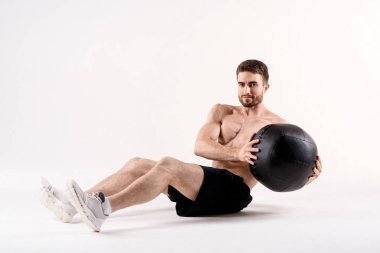 Spor fiziğinde sakallı genç bir adam beyaz tenli arka planda yerden şınav çekiyor, sporcu spor için içeri giriyor.