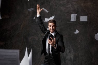 Telefon aracılığıyla iş yapma kavramı. CRM sistemleri ve yenilikçi teknolojiler. Kağıt üzerinde iş yapamamak. Genç adam telefon ekranına bakarak bir yığın belge fırlatıyor.