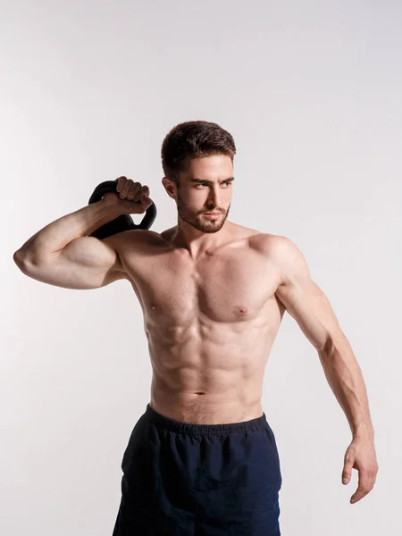 Atleta jovem em um fundo branco levanta um kettlebell. treinamento de um homem barbudo atlético construir — Fotografia de Stock