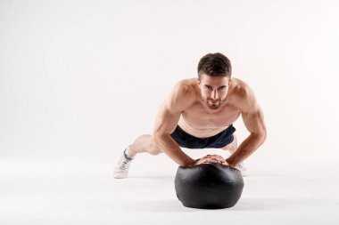 Spor fiziğinde sakallı genç bir adam beyaz tenli arka planda yerden şınav çekiyor, sporcu spor için içeri giriyor.