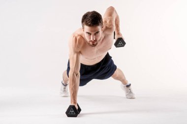 Beyaz izole edilmiş arka planda bir adam dambıllarıyla yere doğru itiyor. Sakallı vücut geliştirme sporcusu.