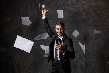 Telefon aracılığıyla iş yapma kavramı. CRM sistemleri ve yenilikçi teknolojiler. Kağıt üzerinde iş yapamamak. Genç adam telefon ekranına bakarak bir yığın belge fırlatıyor.