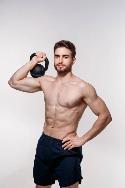 Atleta jovem em um fundo branco levanta um kettlebell. treinamento de um homem barbudo atlético construir — Fotografia de Stock