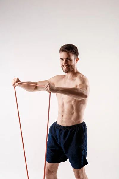Ung sportig man med skägg på vit bakgrund med gymnastiska elastiska band i händerna. träning med gummiband — Stockfoto