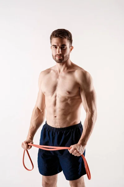 Jovem desportivo com barba sobre fundo branco com elásticos de ginástica nas mãos. treinamento com elásticos — Fotografia de Stock