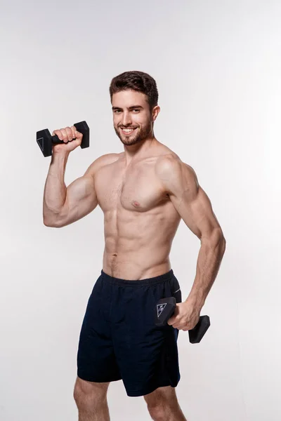 Jovem atleta em um fundo branco levanta halteres. treinamento de um homem barbudo atlético construir — Fotografia de Stock