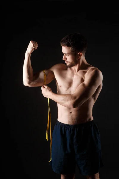 Stark muskulös man som mäter biceps. Muskulös man mäter sin biceps närbild. Naken idrottare med måttband. Viktminskning, hälsosam livsstil — Stockfoto