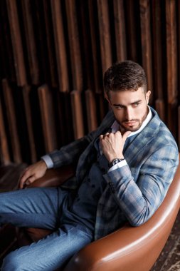 Mavi takım elbiseli başarılı genç işadamı deri bir sandalyede oturuyor. Sakallı genç adam gülümsüyor..