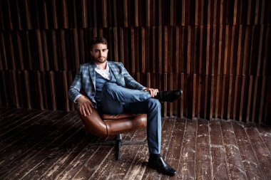 Mavi takım elbiseli başarılı genç işadamı deri bir sandalyede oturuyor. Sakallı genç adam gülümsüyor..