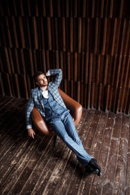 Mavi takım elbiseli başarılı genç işadamı deri bir sandalyede oturuyor. Sakallı genç adam gülümsüyor..