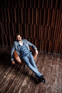 Mavi takım elbiseli başarılı genç işadamı deri bir sandalyede oturuyor. Sakallı genç adam gülümsüyor..