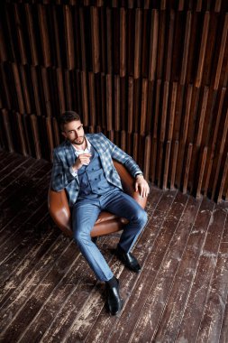 Mavi takım elbiseli başarılı genç işadamı deri bir sandalyede oturuyor. Sakallı genç adam gülümsüyor ve uzaklara bakıyor.