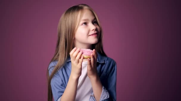 Mała dziewczynka je pączki na różowym tle. dziecko lubi słodycze — Wideo stockowe