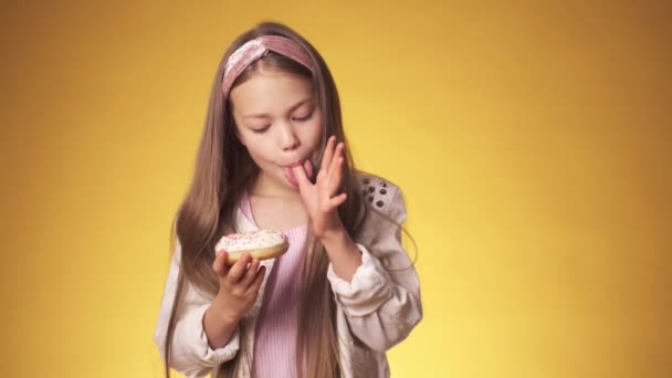 Маленька дівчинка їсть пончики на жовтому тлі. дитина насолоджується цукерками — стокове відео