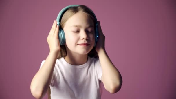 Petite fille écoute de la musique à travers des écouteurs, un enfant danse sur la musique sur un fond rose — Video