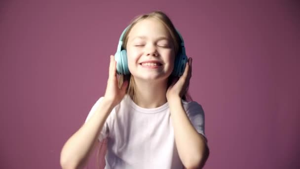 Petite fille écoute de la musique à travers des écouteurs, un enfant danse sur la musique sur un fond rose — Video